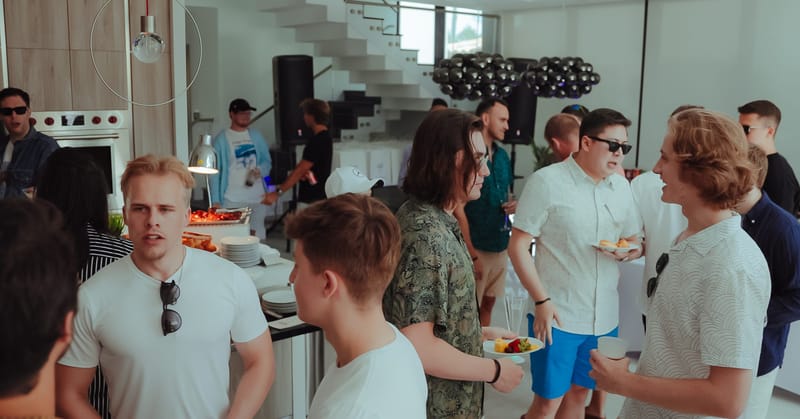 Guests talking in a white modern kitchen, with black balloons on a floating staircase behind