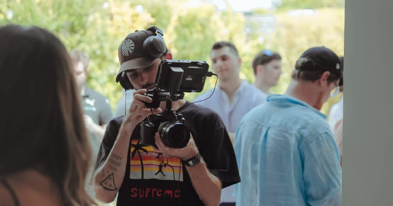 Videographer filming with a camera rig among guests outdoors in the sun