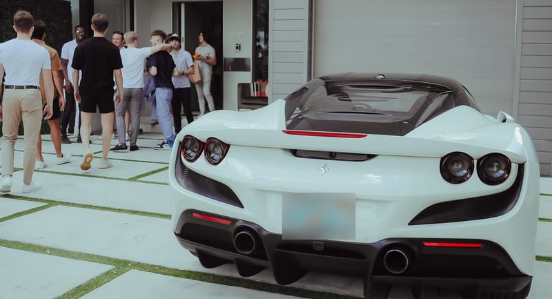 White Ferrari convertible parked on a paved driveway as guests walk toward the house