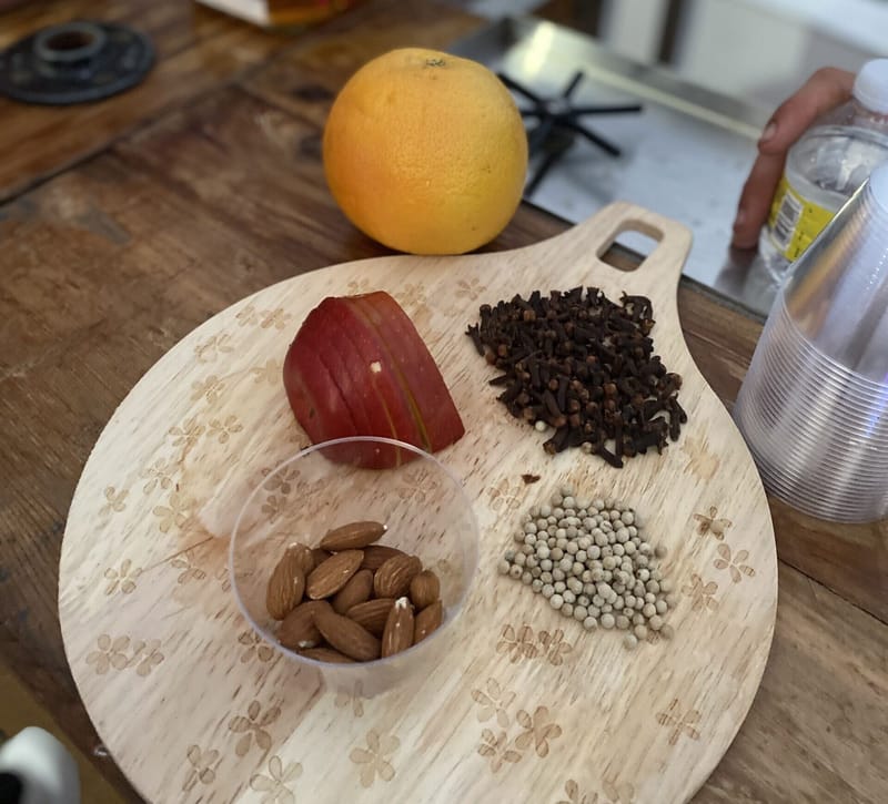 Wooden board with an orange, a sliced apple, cloves, almonds and small pale seeds