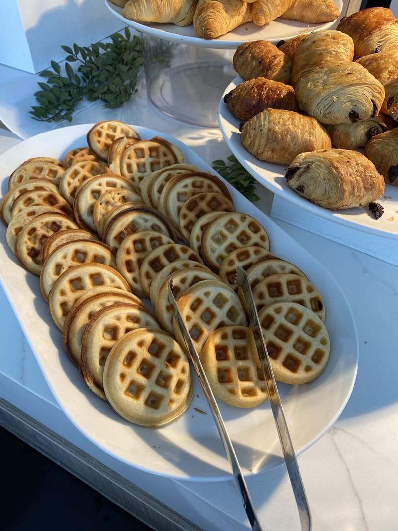 Platter of small waffles with tongs beside a tray of chocolate croissants