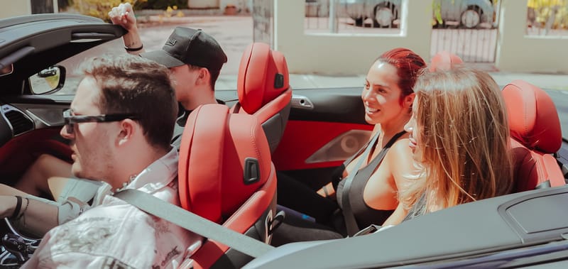 Four guests laughing in a convertible with red leather seats